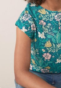 Kortærmet grøn bluse med blomsterprint, der fremviser indviklede rosa og gule mønstre. Blusen har en løs pasform og rund halsudskæring. Stoffet ser blødt og tekstureret ud.