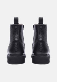 Stivaletti neri in pelle con una superficie testurizzata, pannelli elastici laterali e suola in gomma nera. Presentano un pull tab sul retro e cerniere.