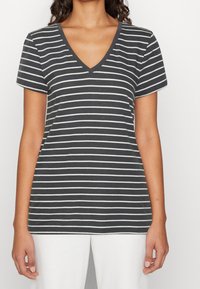 Camiseta gris de cuello en V con rayas horizontales blancas. Manga corta y textura de tela suave. Se lleva con pantalones blancos para un contraste.