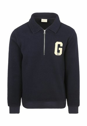 Marineblauwe fleece trui met kraag, halve rits aan de voorkant, geribde manchetten en een groot wit "G" embleem op de linkerborst.