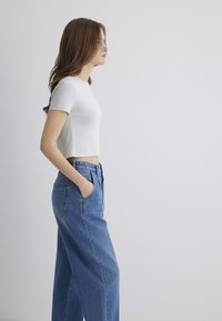 White ribbed crop top with short sleeves paired with high-waisted, loose blue denim jeans featuring side pockets and a classic cut.