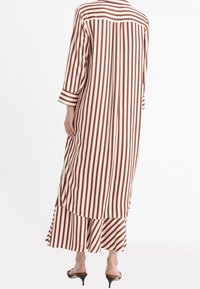 Lång, lätt klänning med röda och vita vertikala ränder, med en knäppt krage och trekvartslånga ärmar, samt en svävande delad design.