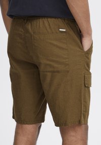 Brune cargo shorts lavet af struktureret stof, med sidelommer og en baglomme med en lille metallisk detalje. Elastisk talje.