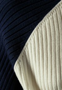 Ribbad tygtröja med en marinblå del och en krämfärgad del med vertikala åsar, vilket visar på kontrasterande texturer.