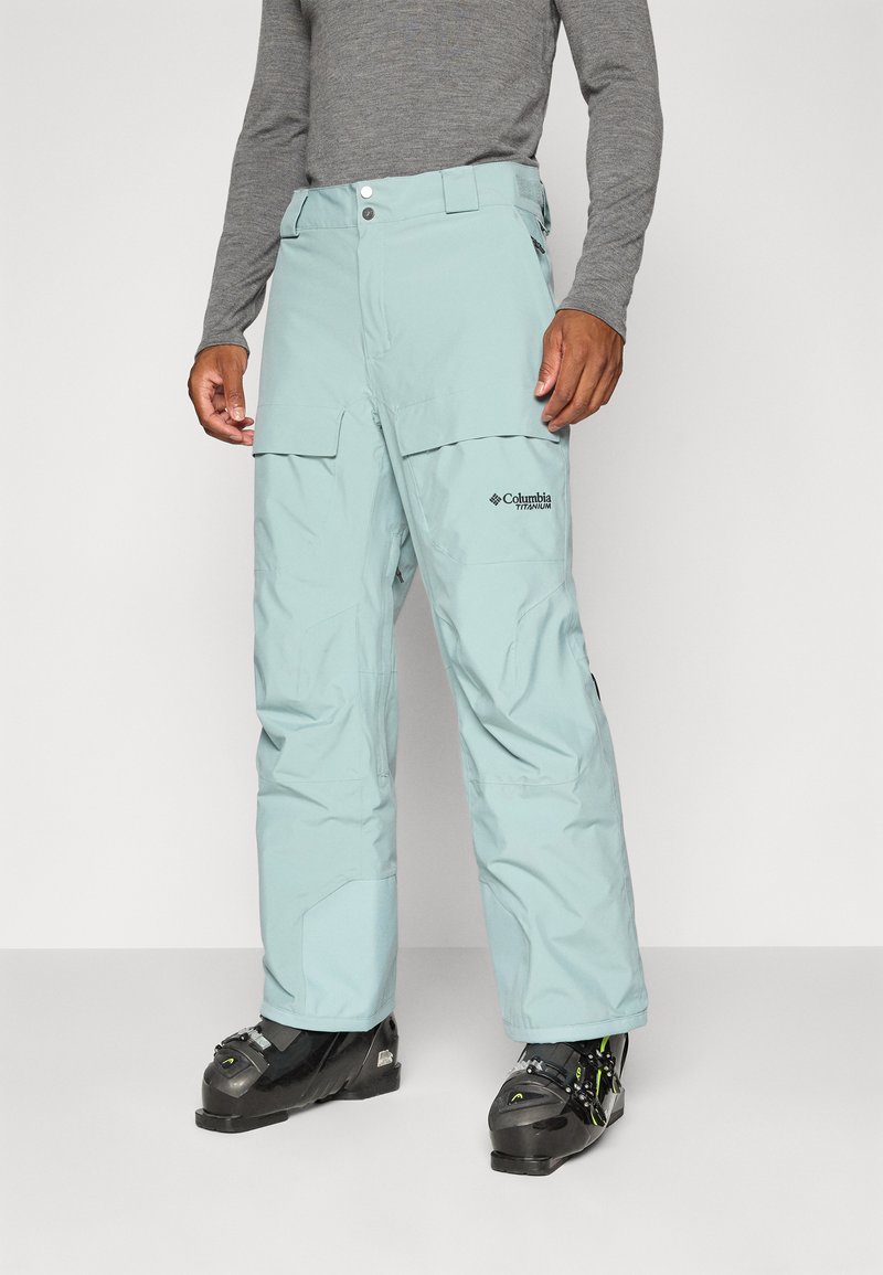 Pantaloni de schi de culoare teal deschis, cu o croială relaxată, fabricați din material rezistent la apă. Prezintă buzunare cargo și branding Columbia Titanium.