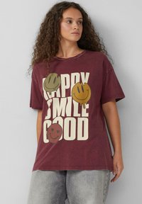 Bordowa bawełniana koszulka z luźnym krojem, z nadrukiem graficznym przedstawiającym trzy uśmiechnięte buźki oraz tekstem "HAPPY SMILE GOOD" w kolorze kremowym.