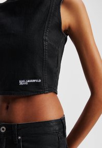 Top scurt din denim negru, cu design fără mâneci, având un logo brodat "KARL LAGERFELD JEANS" în alb, care evidențiază o textură netedă.