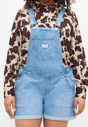 LYSE BLAUE DENIM OVERALLS MED JUSTERBARE STROPPE, FORLØBNINGSLOMME OG SIDEKNAPPER, PARRET MED EN BRUN OG BEIGE MØNSTRET SKJORTE.