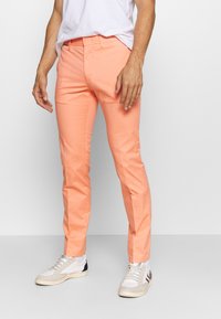 Pantaloni leggeri e su misura di colore corallo brillante, realizzati in cotone. Presentano una vita piatta, tasche laterali e una vestibilità slim, abbinati a sneakers bianche.