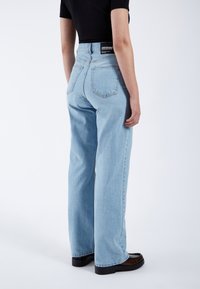 Pantalones vaqueros de tiro alto en azul claro con corte recto, que cuentan con bolsillos traseros y una etiqueta de marca negra en la cintura.