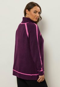 Lila Strickpullover mit hohem Kragen, rosa Akzenten entlang der Ärmel und dem Saum, weicher Textur und lockerer Passform.