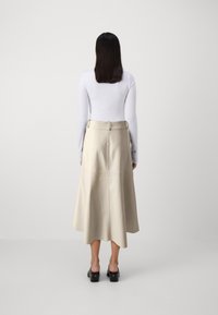 Jupe en cuir beige au design évasé, avec des détails de boucle sur le côté et une couture au centre. Portée avec un haut ajusté à manches longues blanc et des mules à plateforme.