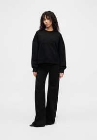 Black oversized sweatshirt with textured chest detail, paired with high-waisted black wide-leg pants. Smooth, soft fabric, casual fit.