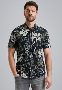 Camisa de manga corta en azul marino con estampado floral en blanco y verde; cuenta con un cuello abotonado y un pequeño logo en el pecho. Hecha de algodón.