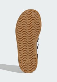 Gumová podrážka s vlnkovým vzorem, s texturovanými gripy. Na bocích jsou viditelné černobílé akcenty.