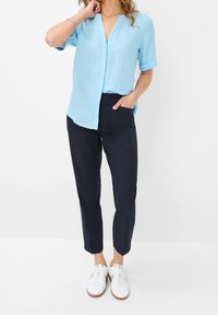 Himmelblaues Leinenhemd mit kurzen Ärmeln und V-Ausschnitt, kombiniert mit navy Slim-Fit-Hosen und weißen Sneakers mit silberner Akzentuierung.