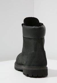 Stivale alla caviglia in pelle nera con una texture liscia, colletto imbottito e suola in gomma resistente. Presenta cuciture visibili e dettaglio del logo.
