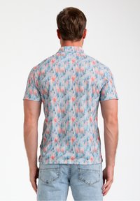 Camisa de manga corta con fondo azul claro y un patrón floral y geométrico en rosa y verde, hecha de una tela suave.