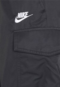 Black fabric cargo pants featuring a white embroidered Nike logo, a patch pocket, and visible stitching details. Smooth texture with minimal sheen.