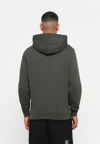 Mørkegrøn hoodie lavet af blødt materiale, med en stor hætte, ribbede manchetter og en afslappet pasform. Ingen synlige logoer eller mønstre.