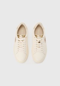 Tenisice krem boje sa zlatnim detaljima, glatkim tekstilnim gornjim dijelom, okruglim vrhom, ravnim vezicama i diskretnim brendiranjem na jeziku i bočnoj strani.