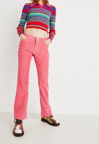 Suéter recortado de canalé colorido en rayas rojas, verdes y azules; combinado con pantalones de pana rosa acampanados; zapatos con patrón y cordones.
