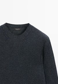 Pullover scuro a coste con scollatura rotonda e etichetta. La texture è morbida con spessore variabile nelle costine.