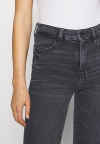 Dark gray high-waisted jeans with a fitted design, featuring front pockets and belt loops, made of denim with a slight sheen.