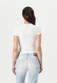White short-sleeve shirt with a round neckline, paired with light blue high-waisted jeans featuring a patch logo and back pockets.