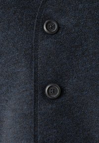 Primo piano di un tessuto di lana blu scuro con due bottoni neri a quattro fori, che mette in evidenza la trama e i dettagli delle cuciture.