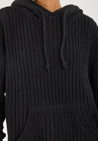 Zwarte gebreide hoodie met een gestructureerde stof, een trekkoordkap en een voorvak voor functionaliteit en warmte.