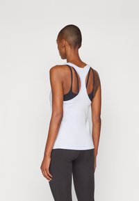 Helehall hallituskollane sportlik tank top, millel on rattakujuline disain ja lõikega detail. Kompondis musta spordibri ja mustade retuusidega. Sile kangast tekstuur.