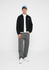 Svart zip-up jacka, vit t-shirt, grå jeans och vita sneakers. Ljusblå keps med en logotyp. Slät, lättviktsmaterial, avslappnad passform.