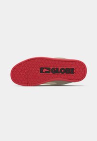 Semelle en caoutchouc rouge avec motif floral texturé et logo noir "GLOBE" sur une chaussure beige sur fond blanc.