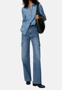 Lichtblauw denim shirt met een kraag, gecombineerd met een wijde blauwe spijkerbroek met zijzakken. Een zwarte leren tas en zwarte laarzen maken de look compleet.
