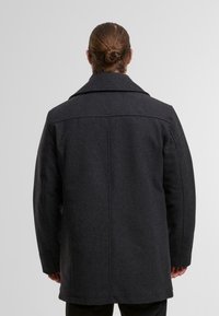 Cappotto grigio scuro con collo strutturato, realizzato in lana, con una linea dritta, tessuti sottili e elementi di design minimalisti.