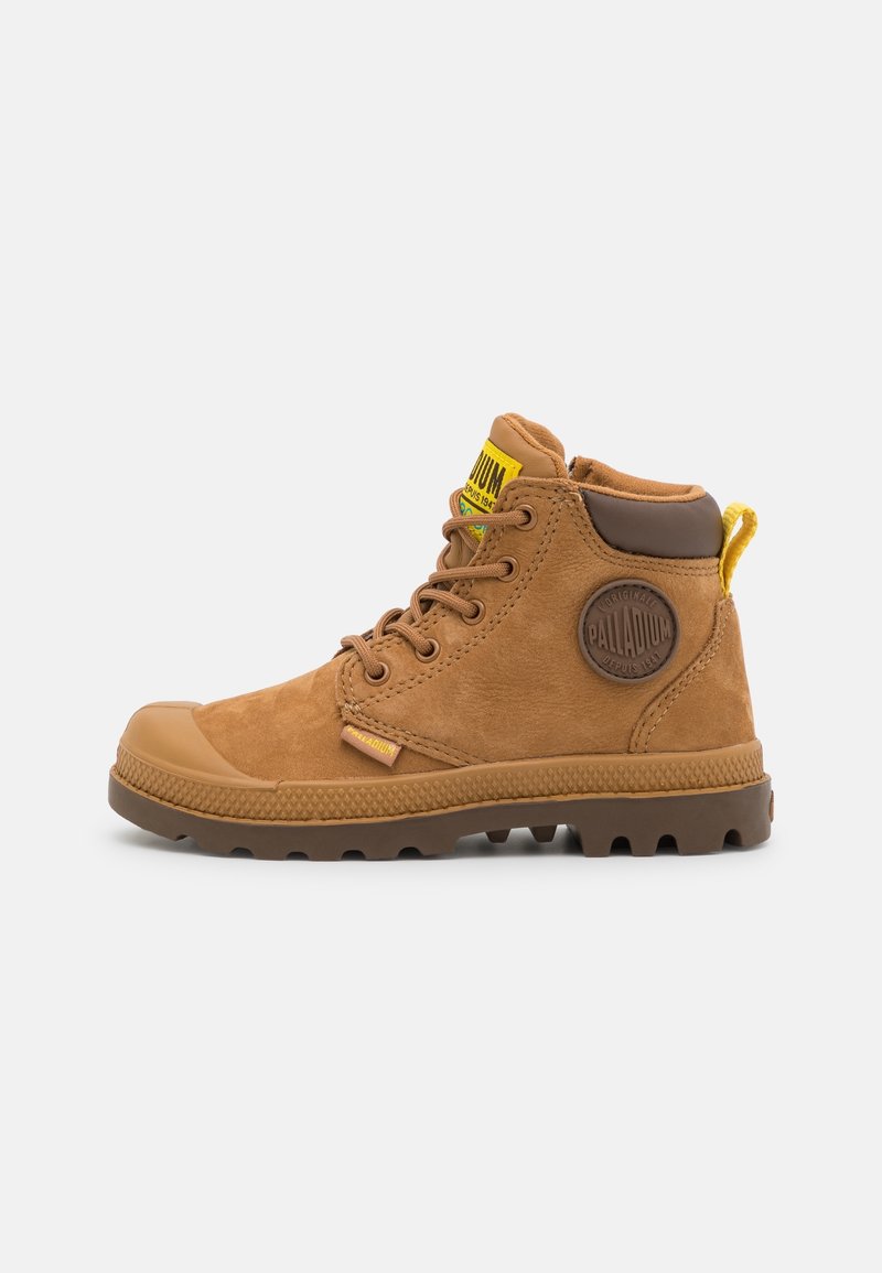 Bottines en daim marron avec semelle en caoutchouc, bout rond, col rembourré, étiquette logo jaune et accents marron texturés.