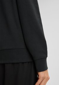 Czarna bawełniana bluza z prążkowanymi mankietami i ściągaczem u dołu. Gładka faktura, luźny krój, charakteryzująca się czystym, minimalistycznym designem.