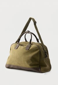 Sac de voyage en toile vert olive avec des accents en cuir brun foncé, doté d'une fermeture éclair, de deux poignées supérieures et d'une bandoulière réglable.