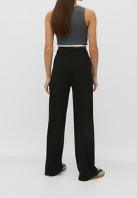 Black wide-leg trousers with a high waist, smooth texture, and a subtle sheen. Paired with a gray cropped tank top and low-profile footwear.