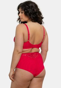 Ensemble de lingerie rouge comprenant un soutien-gorge avec bordure en dentelle et bretelles réglables, ainsi que des culottes taille haute. Tissu lisse avec une coupe ajustée.
