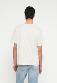 Kremasta pamucna majica kratkih rukava s okruglim izrezom i ležernim krojem. Stražnja strana ima jednoličnu, glatku teksturu.