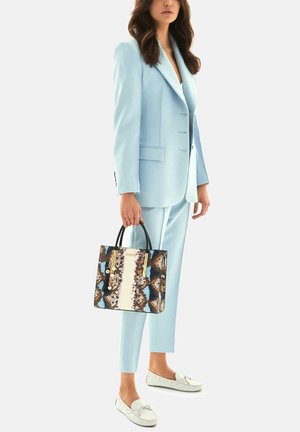 Completo su misura azzurro chiaro abbinato a una borsa a mano con motivo caratterizzato da accenti blu, marroni e crema. Mocassini bianchi completano il look.