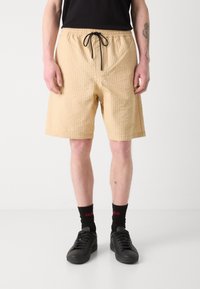 Beige textured shorts with an elastic waistband and black drawstring; paired with black socks and shoes. Simple design, relaxed fit.