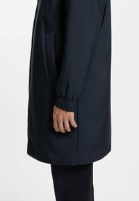 Abrigo largo de color azul marino oscuro, fabricado con un material liso y resistente al agua. Cuenta con puños elásticos y bolsillos laterales para mayor funcionalidad.