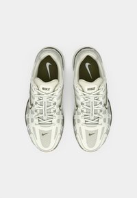 Λευκά sneakers Nike με πλέγμα και συνθετικό επάνω μέρος, με γκρι λεπτομέρειες και χαρακτηριστικό σχέδιο πατούσας στη σόλα. Τα κορδόνια είναι τοποθετημένα στο κέντρο.