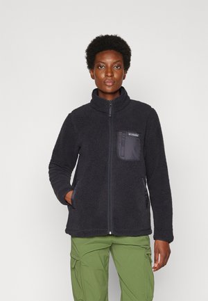 Veste en polaire noire avec un col haut, une fermeture éclair complète et une poche poitrine. Elle présente un tissu texturé et des poches latérales, associée à un pantalon cargo vert.