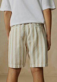 Shorts rayés beige clair et blancs avec une surface texturée, dotés d'une poche arrière et d'une taille élastique, vus de dos.