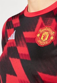 Červená a čierna dres Manchester United s geometrickým vzorom, s okrúhlym výstrihom a vyšívaným logom. Vyrobené z ľahkého syntetického materiálu.
