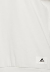 Witte geribde stoffen sweatshirt met een ronde hals, voorzien van een klein zwart Adidas-logo label aan de onderzijde. Zachte textuur, casual ontwerp.